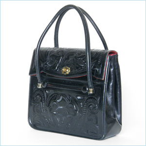 black leather bag with top flap closure and elaborate, tooled floral decoration